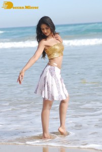 Ileana D’Cruz in a gold top and white skirt walking on the beach
