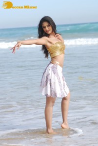 Ileana D’Cruz in a gold top and white skirt walking on the beach