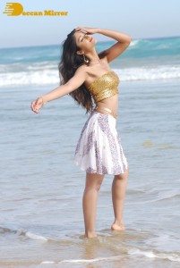 Ileana D’Cruz in a gold top and white skirt walking on the beach