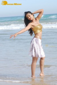 Ileana D’Cruz in a gold top and white skirt walking on the beach