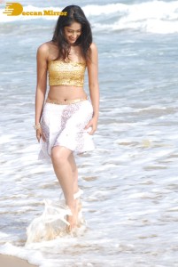 Ileana D’Cruz in a gold top and white skirt walking on the beach