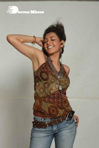 Kajal Aggarwal in a brown top and blue jeans listening to music with headphones from a cell phone