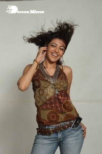 Kajal Aggarwal in a brown top and blue jeans listening to music with headphones from a cell phone