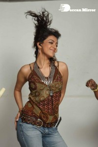 Kajal Aggarwal in a brown top and blue jeans listening to music with headphones from a cell phone