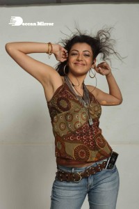 Kajal Aggarwal in a brown top and blue jeans listening to music with headphones from a cell phone
