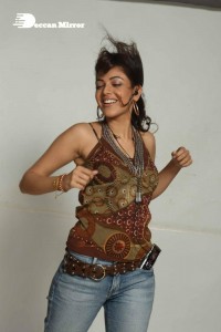 Kajal Aggarwal in a brown top and blue jeans listening to music with headphones from a cell phone