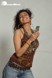 Kajal Aggarwal in a brown top and blue jeans listening to music with headphones from a cell phone