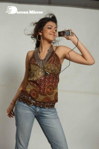 Kajal Aggarwal in a brown top and blue jeans listening to music with headphones from a cell phone