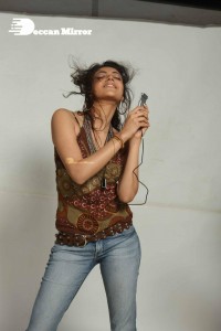 Kajal Aggarwal in a brown top and blue jeans listening to music with headphones from a cell phone