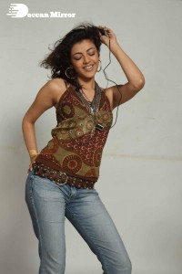 Kajal Aggarwal in a brown top and blue jeans listening to music with headphones from a cell phone