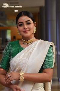 Actress Poorna in a white saree and green blouse posing for a photoshoot
