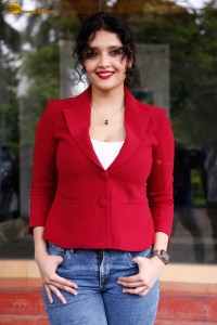 actress Ritika Singh in a red coat and blue denim jeans