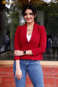 actress Ritika Singh in a red coat and blue denim jeans