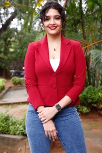 actress Ritika Singh in a red coat and blue denim jeans