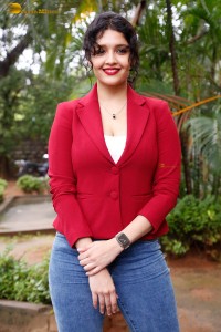 actress Ritika Singh in a red coat and blue denim jeans