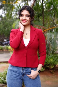 actress Ritika Singh in a red coat and blue denim jeans